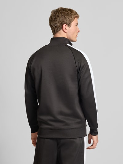 Männermodel trägt Sweatjacke mit Label-Print von PUMA PERFORMANCE, Material-Mix mit Baumwoll-Anteil, Regular-Fit, Stehkragen, Reißverschluss, Reißverschlusstaschen, gerippte Abschlüsse, Rückenlänge bei Größe M 73 cm, Ärmellänge 52 cm, schwarze Farbe mit weißen Streifen, glatte Textur, Ganzkörperansicht Rückansicht.