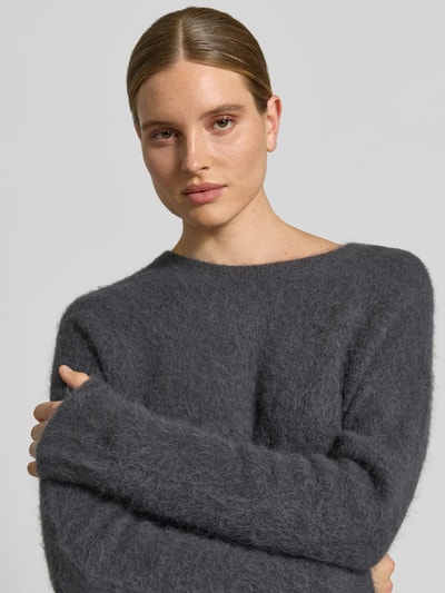 Vrouwenmodel draagt Wollpullover aus Alpaka-Woll-Mix van Juvia in donkergrijs, tricotlook, los model, ronde hals, elastisch, Nahaufnahme bovenlichaam. Ruglengte maat S: 57 cm, borstwijdte: 50 cm, mouwlengte: 62 cm.