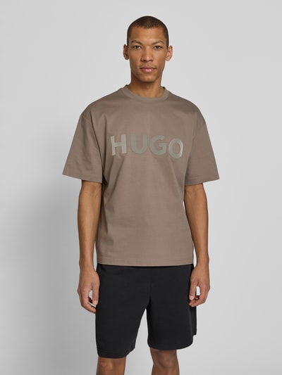 Männermodel trägt Relaxed Fit T-Shirt aus reiner Baumwolle Modell 'DINKEE' von HUGO, unifarben, 3D Label Print, Jersey, Ganzkörperansicht von vorne.