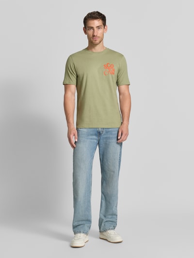 Männermodel trägt Regular Fit T-Shirt mit Logo-Print von Scotch & Soda in Grün aus reiner Baumwolle, Rundhalsausschnitt, Ganzkörperansicht von vorne.
