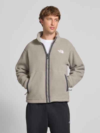 Männermodel trägt Regular Fit Fleecejacke mit Logo-Stitching von The North Face in Beige mit Stehkragen, Reißverschluss, Eingrifftaschen, Nahaufnahme Oberkörper.