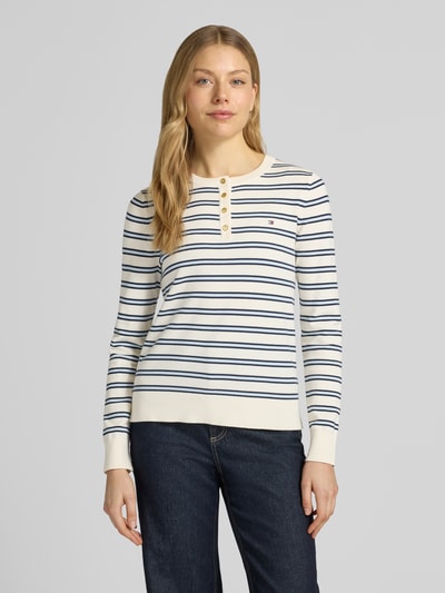 Vrouwenmodel draagt Regular Fit Langarmshirt aus Baumwoll-Mix van Tommy Hilfiger, gestreept all-over motief, katoenmix knitwear, henley-hals, geribde boorden, gestikt logo, regular fit pasvorm, gebreide textuur, lichte kleur met blauwe strepen, ganzekörpervanvooraanzicht