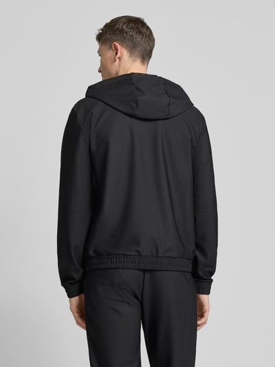 Männermodel trägt Regular Fit Sweatjacke mit Logo-Patch von EA7 Emporio Armani, Schwarz, Strukturmuster, Rückansicht, Ganzkörperansicht. Elastischer-Material-Mix, Kapuze mit Tunnelzug, Eingrifftaschen, Zweiwege-Reißverschluss, elastische Abschlüsse, Rückenlänge 68 cm, Ärmellänge 67 cm, Größe M.