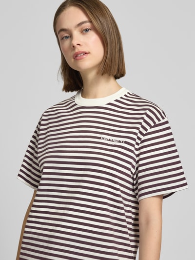 Modelka kobieca nosi T-Shirt mit Label-Stitching od Carhartt Work In Progress, białe i bordowe paski, bawełna, krój relaxed fit, model 'Ezra', okrągły dekolt, damska koszulka, widok na górną część ciała z przodu.