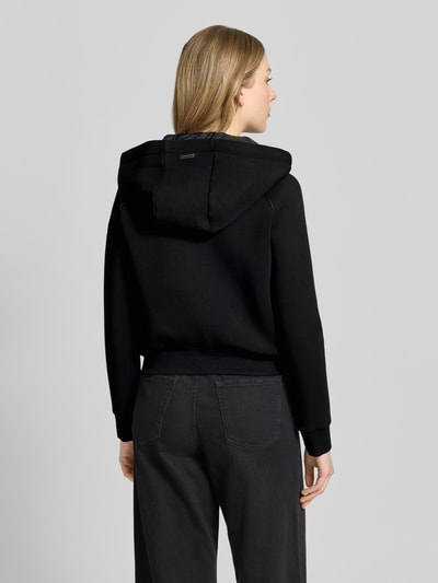 Frauenmodel trägt schwarze Steppjacke mit Kapuze, Reißverschlusstaschen, Regular-Fit, Modell 'MALAYA' von khujo, Ganzkörperansicht Rückansicht, Rückenlänge bei Größe S 50 cm, Schulterbreite 47 cm, Brustweite 49 cm, Ärmellänge 71 cm.
