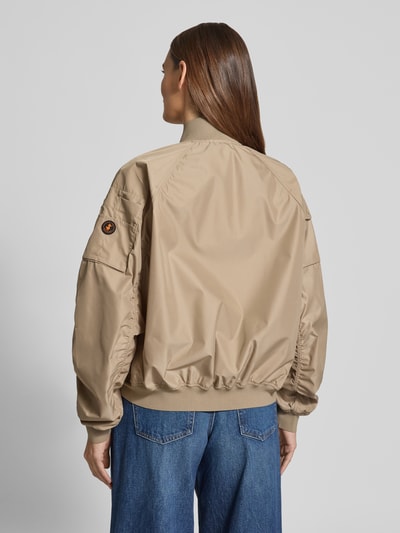 Vrouwenmodel draagt Bomberjack met ritszakken model 'LIL' van SAVE THE DUCK, beige materiaalmix met stretch, regular fit, ruglengte maat S 53 cm, schouderbreedte 42 cm, borstwijdte 61 cm, mouwlengte 70 cm, opstaande kraag, achterkant volledig zichtbaar, geheelopname rugaanzicht.