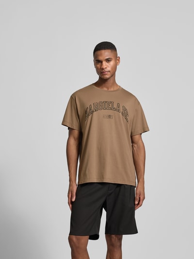 Männermodel trägt Regular Fit T-Shirt mit Logo-Print von MM6 Maison Margiela in Braun, reine Baumwolle, Rundhalsausschnitt, Statement-Print, Ganzkörperansicht von vorne.