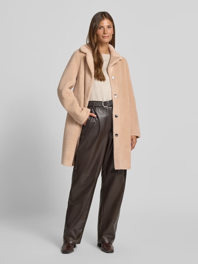 Frauenmodel trägt Wendemantel in Woll-Lammfell-Optik Modell 'VENUS' von OAKWOOD in Beige, lockere Passform, Reverskragen, Eingrifftaschen, Ganzkörperansicht von vorne. Rückenlänge 89 cm, Schulterbreite 44 cm, Brustweite 50 cm, Ärmellänge 62 cm.