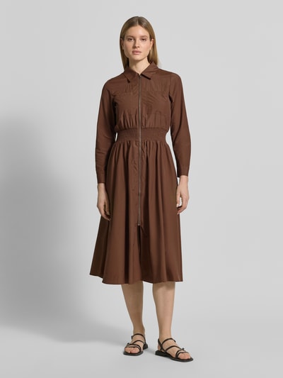 Frauenmodel trägt Hemdblusenkleid mit Reißverschluss Modell 'NETTI' von Soyaconcept aus braunem Material-Mix mit Baumwoll-Anteil, A-Linie, Elastisch, Midikleid, Taillenband, Rückenlänge bei Größe S 121 cm, Brustweite 42 cm, Ärmellänge 60 cm, Ganzkörperansicht von vorne.