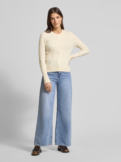 Kobiece modelka nosi Regular Fit Strickjacke mit Viskose-Anteil Modell 'FANTASTIC' od Vero Moda, kremowy sweter z okrągłym dekoltem, wzór warkoczowy, długie rękawy, prążkowane ściągacze, prosta jednorządowa lista guzikowa, widok całej sylwetki z przodu.