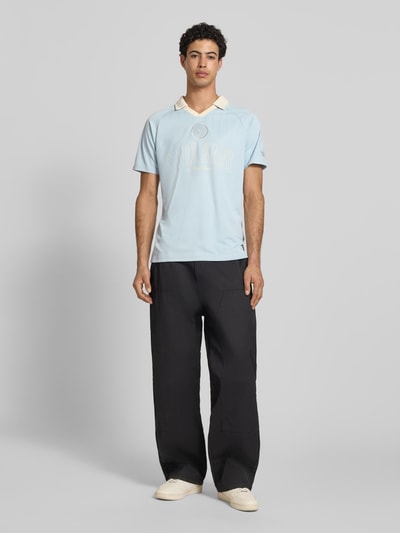 Männermodel trägt Regular Fit T-Shirt mit Umlegekragen Modell 'Heritage' von KARL KANI, hellblau mit Logo-Stitching, Rückenlänge 70 cm, Ganzkörperansicht von vorne.