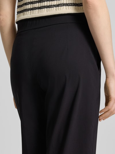 Vrouwenmodel draagt Hose aus Viskose-Mix in verkürzter Passform Modell 'FENJA2' van STEHMANN, zwarte stof, elastische taille, detailopname rugzijde.