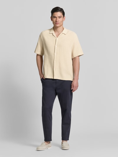 Männermodel trägt Relaxed Fit Freizeithemd aus reiner Baumwolle Modell 'RLXCAL' von SELECTED HOMME, Optik: Unifarben, Hemdkragen: Bowling-Kragen, Knopfleiste: einreihig, Ärmelform: Kurzarm, Material: reine Baumwolle, sanft strukturierte Oberfläche, helle Farbe, Ganzkörperansicht von vorne.