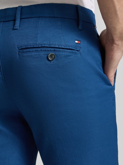 Männermodel trägt Slim Fit Chino aus Baumwoll-Mix von Tommy Hilfiger in Blau mit Logo-Stitching, Piqué-Struktur, Nahaufnahme Hüfte rückseitig.