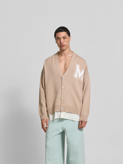 Männermodel trägt Oversized Cardigan aus Schurwoll-Mix von MM6 Maison Margiela in Beige mit V-Ausschnitt, Strick-Optik, Ganzkörperansicht von vorne. Rückenlänge 78 cm, Schulterbreite 48 cm, Ärmellänge 69 cm.