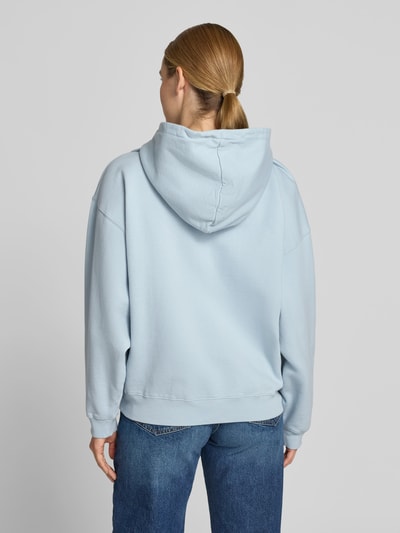 Frauenmodel trägt Relaxed Fit Hoodie mit Logo-Detail von Anine Bing aus reiner Baumwolle in Hellblau mit elastischen Abschlüssen und Känguru-Tasche, Rückenlänge 85 cm bei Größe S, Ganzkörperansicht Rückansicht.