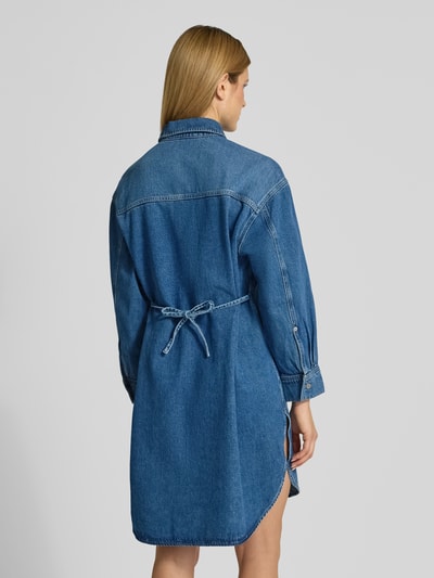 Vrouwenmodel draagt Oversized Jeanskleid aus Lyocell-Mix van Armedangels in denimlook, oversized fit, midilengte, lange mouw, strikceintuur, borstzak, knoopsluiting, rechte zoom, lyocellmix, labelpatch, rugaanzicht, ganzkörperansicht rückansicht.