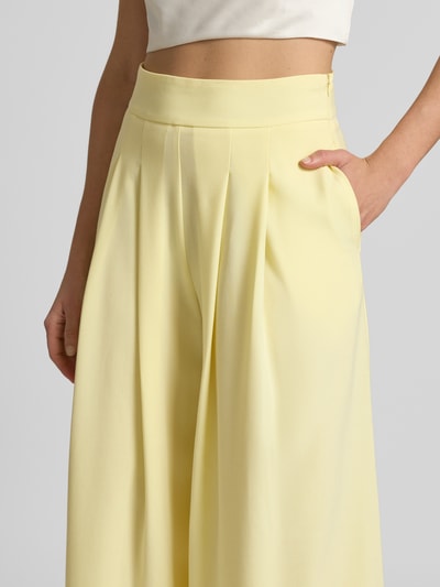 Frauenmodel trägt Hose mit Falten und seitlichem Reißverschluss von Rinascimento in Hellgelb, Material-Mix mit Viskose, Nahaufnahme Oberkörper.