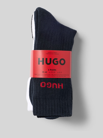 Produktfoto, czarne i białe skarpetki z czerwonym logo HUGO, gładka tekstura, opakowanie na 3 pary, jednokolorowy design