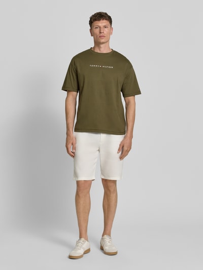 Männermodel trägt Regular Fit T-Shirt aus reiner Baumwolle von Tommy Hilfiger in Olivgrün mit weißem Label Print, kurzarm, Ganzkörperansicht von vorne.