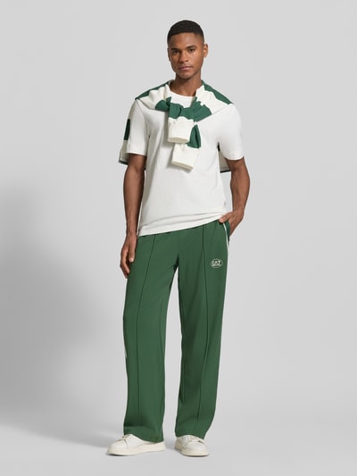 Männermodel trägt Trackpants aus Viskose-Mix von EA7 Emporio Armani in Grün mit Gerade Passform, Elastischer Bund, Ziernähte, Label-Print, Eingrifftaschen, Galonstreifen; Ganzkörperansicht von vorne.
