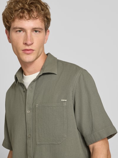 Männermodel trägt Regular Fit Freizeithemd aus reiner Baumwolle von G-Star RAW in Olivgrün, strukturierte Oberfläche, Nahaufnahme Oberkörper.