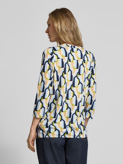 Vrouwenmodel draagt t-shirt met 3/4-mouw model 'FELICITY' van Soyaconcept, katoen- en viscosemix, regular fit, v-hals, ruglengte maat S 63 cm, geometrisch patroon in wit, geel, blauw en beige, rugaanzicht.
