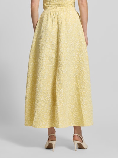 Modelka nosi Ausgestellter Maxi-Rock mit Strukturmuster Modell 'FIONA' od Vero Moda, żółty, strukturalny, krój regular fit, piqué, jacquard, kieszenie boczne, widok całej sylwetki od tyłu.