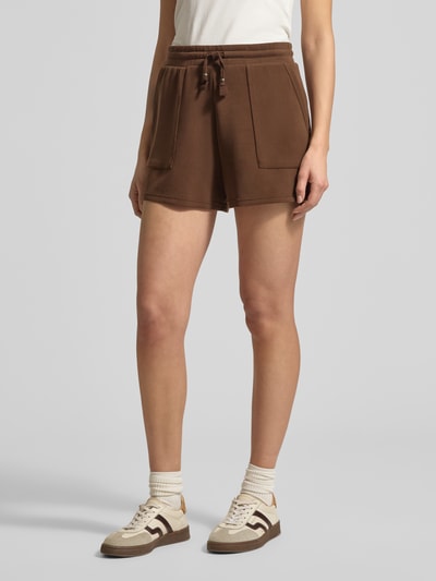 Frauenmodel trägt Sweatshorts mit Seitentaschen von Scotch & Soda in Braun, gerader Schnitt, elastischer Bund, Nahaufnahme Oberschenkel.