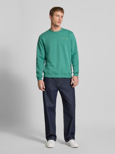 Männermodel trägt Regular Fit Sweatshirt aus Baumwoll-Mix Modell 'LINEAR CREW' von Tommy Jeans in Optik: Unifarben, Ganzkörperansicht von vorne.