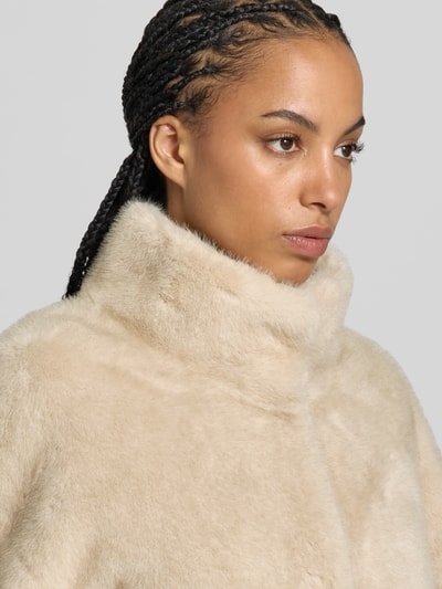 Vrouwenmodel draagt Kunstfelljacke met Stehkragen van Juvia in imitatiebont, licht beige tint, a-lijn, afdekstrip, detailopname bovenlichaam. Ruglengte maat S 80 cm, borstwijdte 50 cm, mouwlengte 62 cm.