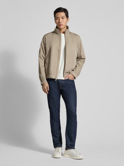 Männermodel trägt Jacke mit Stehkragen und Reißverschluss von CK Calvin Klein in Beige, kombiniert mit Jeans und Sneakers, Ganzkörperansicht von vorne; Regular Fit, Eingrifftaschen, Rückenlänge 65 cm, Schulterbreite 46 cm, Brustweite 57 cm, Ärmellänge 67 cm.