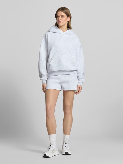 Frauenmodel trägt Hoodie mit Spitzenkanten an Kapuze, Känguru-Tasche und Ärmelbund von Review, heller Material-Mix, Relaxed-Fit, Label-Stitching, Ganzkörperansicht von vorne.