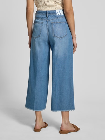 Frauenmodel trägt Wide Leg Culotte-Jeans aus Lyocell-Baumwoll-Mix Modell 'SURI' von s.Oliver RED LABEL in Denim-Optik, Fransen am Beinabschluss, High Waist, 5-Pocket-Design, Logo-Print, Ganzkörperansicht Rückansicht