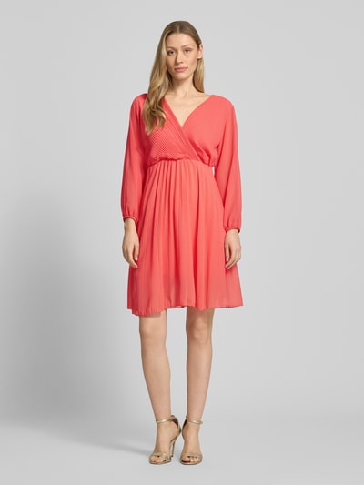 Frauenmodel trägt Kleid aus Viskose-Mix mit V-Ausschnitt von ZABAIONE in koralle, Tailliert, langärmelig, Semitransparent, blickdichter Unterrock, Ganzkörperansicht von vorne. Rückenlänge 94 cm, Brustweite 45 cm, Ärmellänge 56 cm, Größe S.