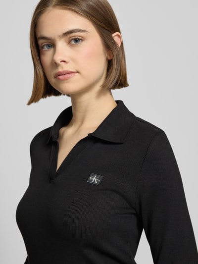 Frauenmodel trägt Longsleeve mit Label-Detail von Calvin Klein Jeans aus schwarzem Baumwoll-Elasthan-Mix, Slim-Fit, Polokragen, V-Ausschnitt, Nahaufnahme Oberkörper.