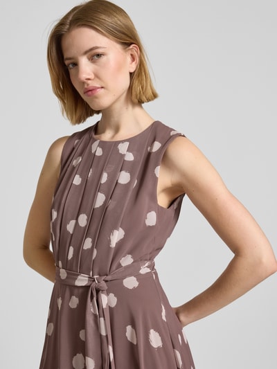 Vrouwenmodel draagt Midikleid mit gelegten Falten van Christian Berg Cocktail in taupe met witte stippen, getailleerde fit, afneembare stoffen riem, ronde hals, mouwloos ontwerp, ondoorzichtige onderjurk, detailopname bovenlichaam.