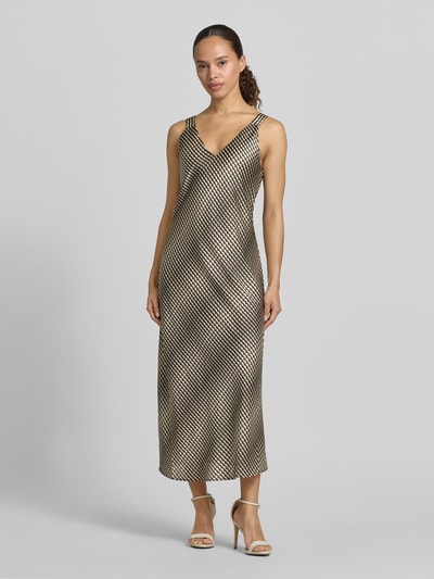 Frauenmodel trägt Midikleid mit V-Ausschnitt Modell 'Qova wave' von Someday, Satin, Straight Fit, schwarz-gold gemustert, Ganzkörperansicht von vorne.