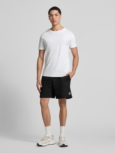 Männermodel trägt Regular Fit Sweatshorts aus Baumwoll-Mix Modell 'TREFOIL ESSENTIALS' von adidas Originals, Optik: Unifarben, Logo-Stitching, Bundabschluss: elastisch, seitliche Eingrifftaschen, Materialverarbeitung: Sweat, Material: Baumwoll-Mix, Ganzkörperansicht von vorne.