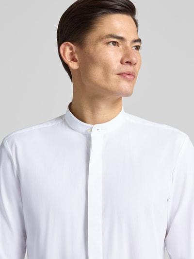 Męski model nosi Slim Fit Businesshemd aus reiner Baumwolle Modell 'KALEB' od HUGO, efekt: jednolity kolor, stójka, długi rękaw, aplikacja z wyhaftowanym logo, zapięcie: listwa guzikowa kryta, wykończenie: zaokrąglone, materiał: bawełna; nahaufnahme górnej części ciała.