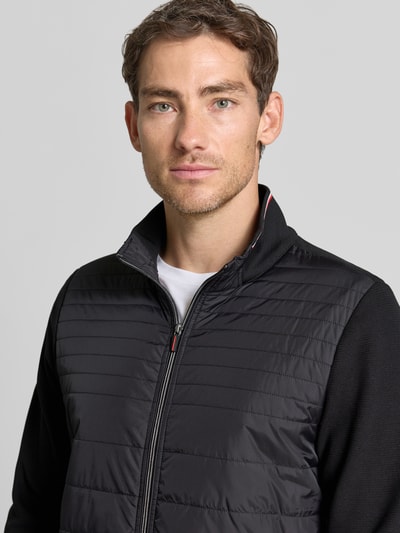 Männermodel trägt Steppjacke aus Baumwoll-Mix von Christian Berg Men, czarny materiał, zamek błyskawiczny, wpuszczane kieszenie, stójka, dopasowany krój, mieszanka bawełny i elastanu, rękawy z dzianiny dresowej, prążkowane wykończenia, długość tyłu 67 cm, długość rękawów 66 cm, Nahaufnahme Oberkörper.