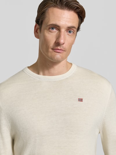 Mężczyzna nosi sweter wełniany z czystej wełny Slim Fit Model 'DAMAVAND' od Napapijri, detal z logo; zbliżenie na górną część ciała.