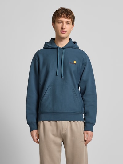 Męskimodel nosi Hoodie mit Kapuze od Carhartt Work In Progress, mieszanka bawełny, luźny krój, kaptur, tunel, wyhaftowane logo, kieszeń kangurka, prążkowane wykończenia, niebieski kolor, długość tyłu 70 cm, długość rękawów 64 cm, widok całej sylwetki z przodu.