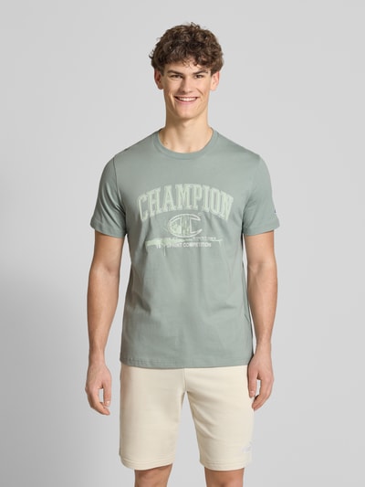 Männermodel trägt T-Shirt mit Label-Print und Rundhalsausschnitt von CHAMPION, reine Baumwolle, krój regular fit, Ganzkörperansicht von vorne