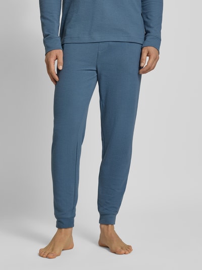 Männermodel trägt Relaxed Fit Pyjama-Hose aus Baumwoll-Mix Modell 'AUSTIN PANTS' von HUGO, niebieski, wafelowa faktura, regular fit, sznurek w pasie, boczne kieszenie, nadruk z logo, unikatowa struktura, Ganzkörperansicht von vorne.
