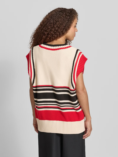Frauenmodel trägt Pullunder mit V-Ausschnitt von Karo Kauer, Reine Baumwolle, Straight Fit, Gerippte-Abschlüsse, Rückenlänge bei Größe S 65 cm, Farbkombination aus Creme, Rot und Schwarz, Struktur mit grobem Strick, Ganzkörperansicht Rückansicht.