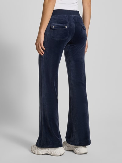 Frauenmodel trägt Low Rise Sweatpants mit elastischem Bund Modell 'LAYLA' von Juicy Couture, dunkelblauer Baumwoll-Mix mit Stretch-Anteil, Flared-Cut, Eingrifftaschen, Ganzkörperansicht Rückansicht.