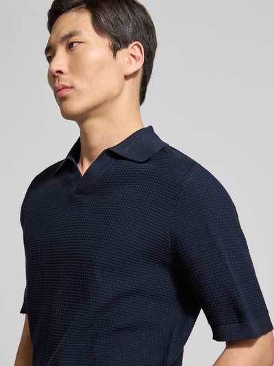 Männermodel trägt Regular Fit Poloshirt aus reiner Baumwolle von Tom Tailor in dunkelblauer Strickoptik mit Strukturmuster, Nahaufnahme Oberkörper.