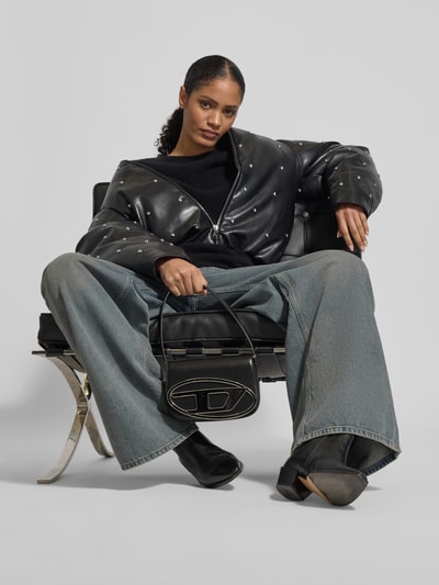 Frauenmodel trägt Shoulder Bag mit Logo-Detail von Diesel, schwarzes Leder, Doppelter Schulterriemen, Magnetverschluss, Ganzkörperansicht von vorne.