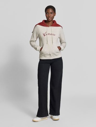 Frauenmodel trägt Hoodie aus reiner Baumwolle von KENZO in Beige mit roter Kapuze, Label-Print, taillierte Passform, Känguru-Tasche, Ganzkörperansicht von vorne.